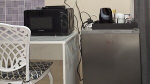 Et værelse med et tv ophængt på væggen, en mikrobølgeovn på et bord, et køleskab, en stol og et gardin.