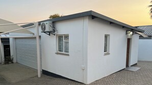 En lille, hvid bygning med en garageport, to vinduer og en aircondition-enhed monteret på den ydre væg.