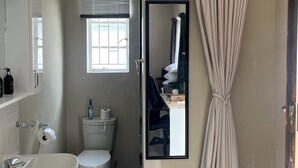 Et badeværelse med toilet, håndvask, spejl og et vindue med rullegardiner.