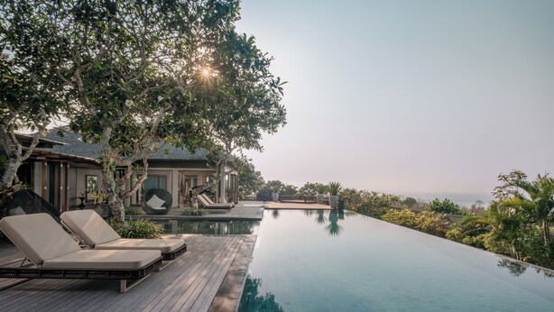 A poolside area with lounge chairs, a wooden deck, and a view of the ocean. - The Shanti Residence By Nakula (Nusa Dua)