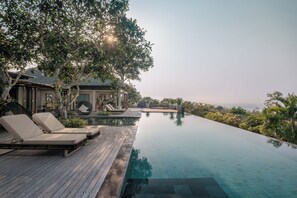 A poolside area with lounge chairs, a wooden deck, and a view of the ocean. - The Shanti Residence By Nakula (Nusa Dua)