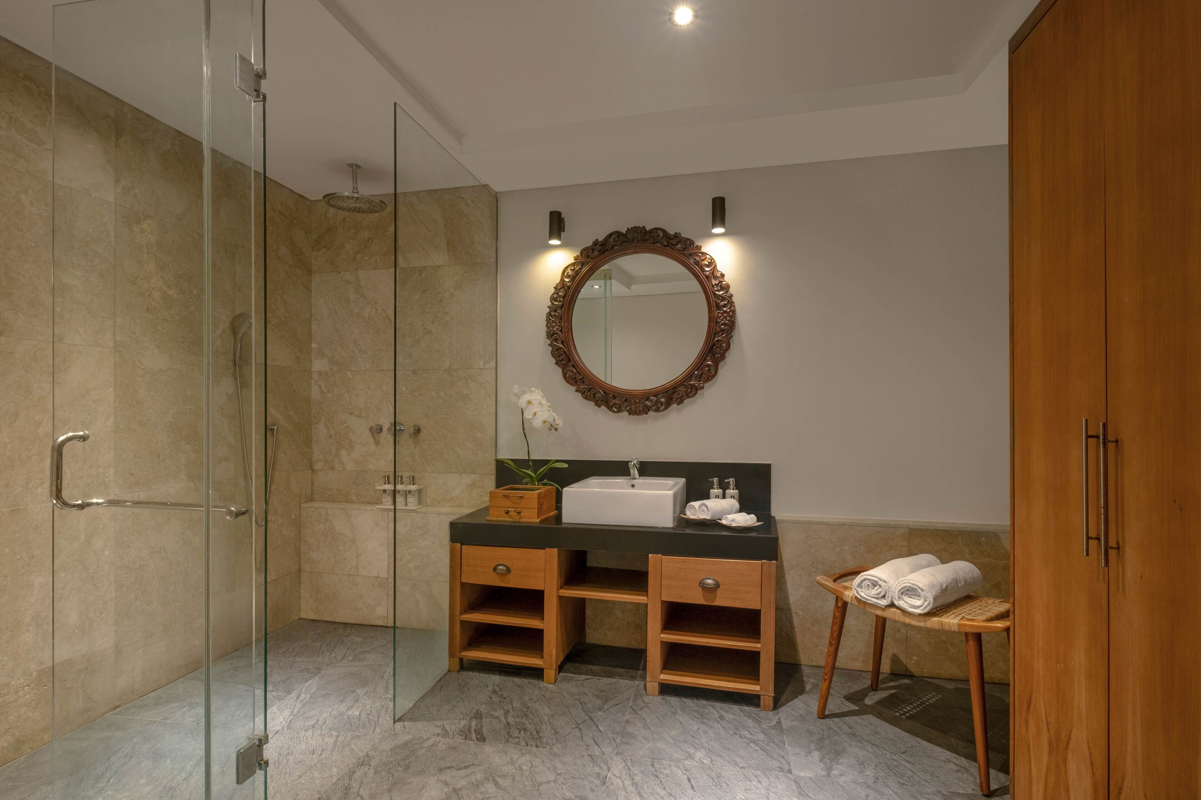 Un bagno moderno con box doccia in vetro, mobile bagno in legno con lavandino, specchio con illuminazione e pensile in legno.