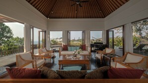 A spacious living area with a high ceiling, large windows, and a view of the outdoors. - The Shanti Residence By Nakula (Nusa Dua)