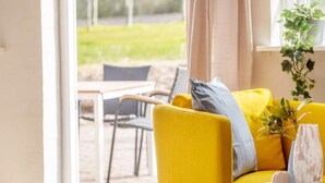 A bright yellow sofa with a grey pillow, a white vase with flowers, and a potted plant on a windowsill. - 4 Star Holiday Home in Hjorring (Hjørring)
