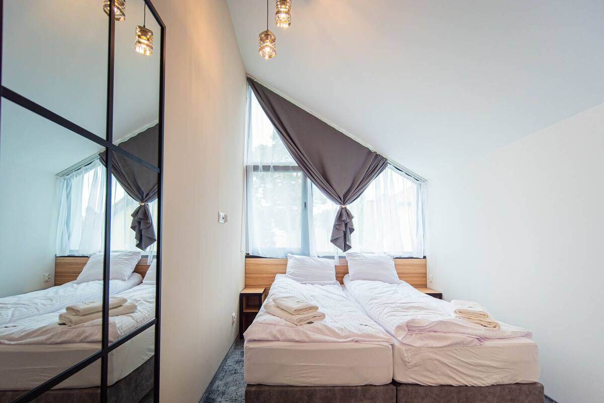 Ein Zimmer mit zwei Betten, einem großen Spiegel und einem Fenster mit Vorhängen.
