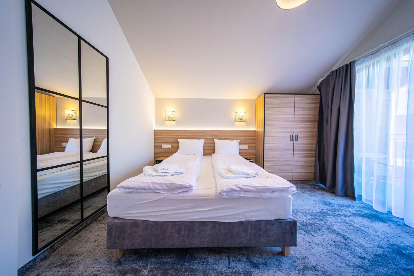Habitación de hotel con una cama grande, un armario, un espejo y una ventana con cortinas.