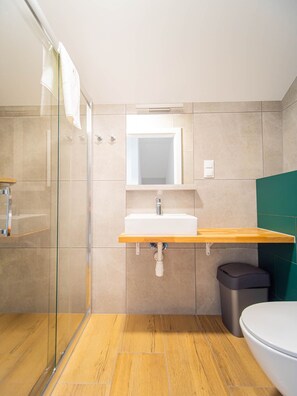 Un bagno moderno con cabina doccia in vetro, lavabo bianco con piano in legno e parete verde.