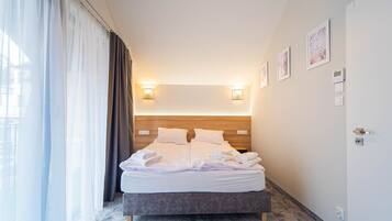 Quarto de hotel com uma cama, duas luzes fixadas na parede, uma porta e uma janela com cortinas.