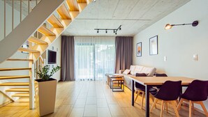 A modern interior with a wooden staircase, a dining area with a table and chairs, a sofa, and a TV mounted on the wall. - Gold Time (Niechorze)