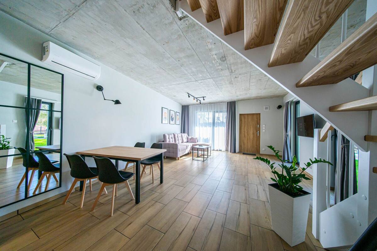 Ein modernes Interieur mit Essbereich, Sofa, Treppe und großen Fenstern.
