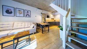 A modern living space with a sofa, dining table, staircase, and kitchen area. - Gold Time (Niechorze)