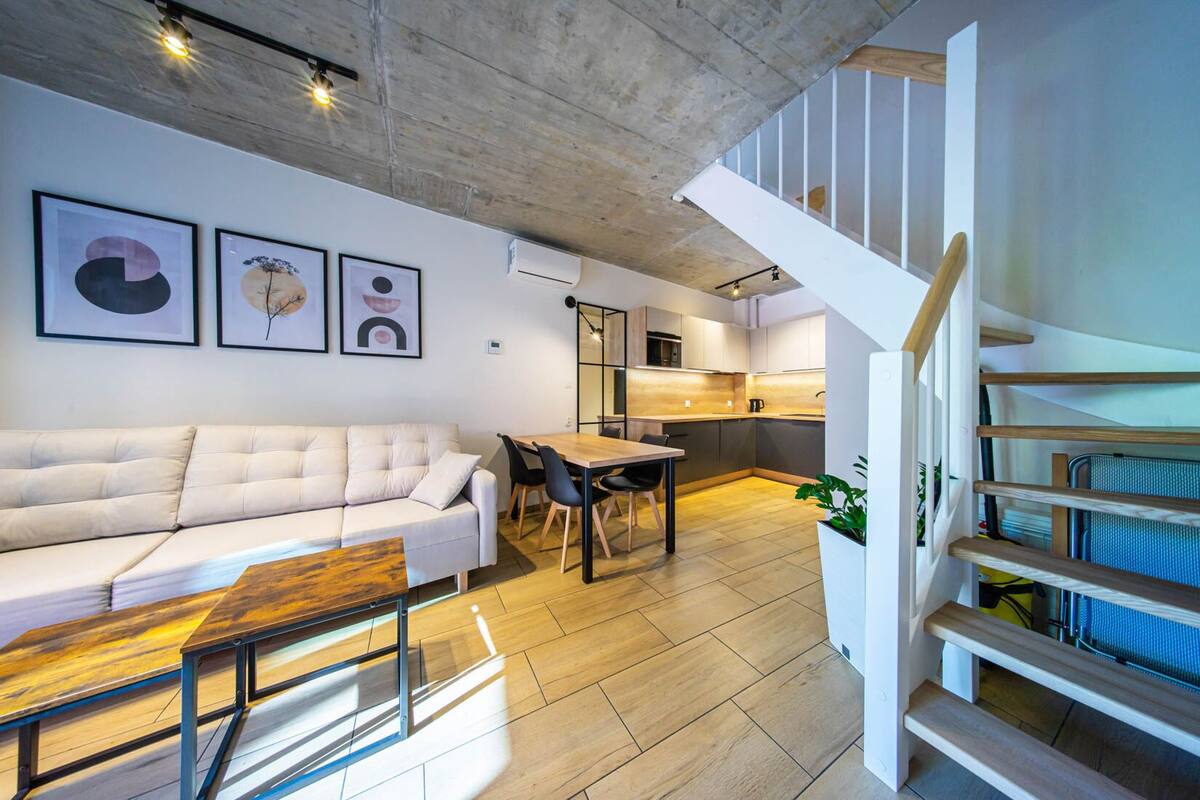 Ein zeitgemäßer Wohnraum mit Sofa, Esstisch, Treppe und Küchenbereich.