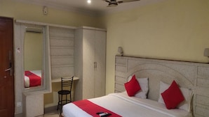 A hotel room with a bed, a chair, a wardrobe, and a ceiling fan. - HARIHARAN RESIDENCY (Chennai)