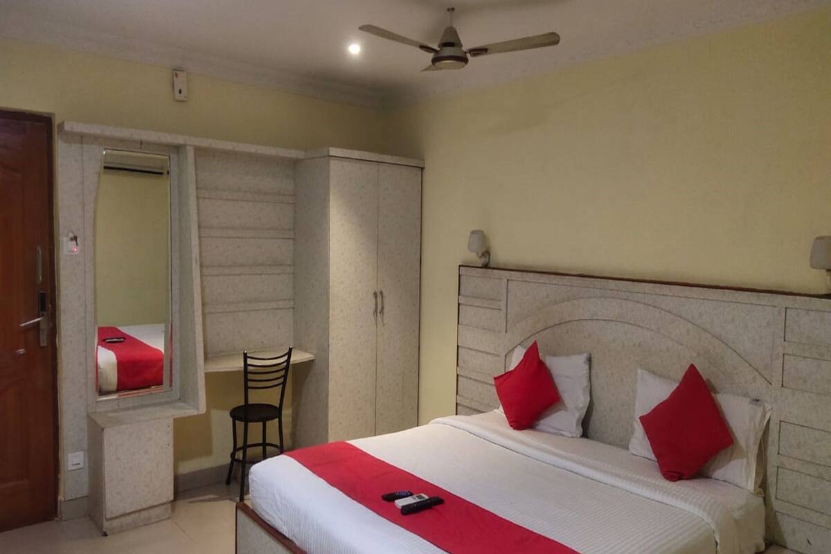 A hotel room with a bed, a chair, a wardrobe, and a ceiling fan.