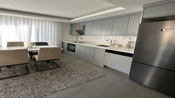A modern kitchen with grey cabinets, a stainless steel refrigerator, and a dishwasher. - SOHO (Alanya)