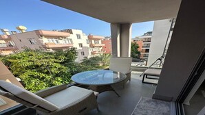 A balcony with wicker furniture, a glass table, and a view of surrounding buildings. - SOHO (Alanya)
