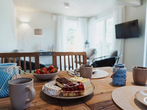 Een eettafel met een bord desserts, een koffiemok en een schaal aardbeien.