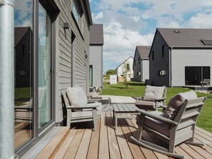 Een terras met buitenmeubilair, een glazen deur en uitzicht op omliggende huizen.
