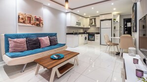A modern living room with a sofa, coffee table, and kitchen area with appliances.