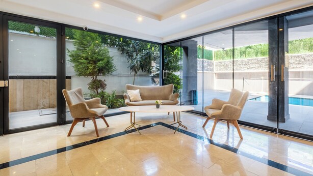 A modern interior with a sofa, two armchairs, a coffee table, and a glass door leading to a pool.