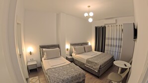 A hotel room with two beds, a small table, a TV, and a ceiling light fixture. - salillari guest house (Vërtop)