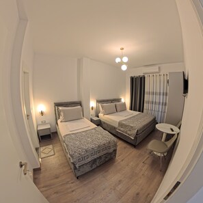 Habitación de hotel con dos camas, una mesita pequeña, televisión e iluminación en el techo.