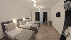 A hotel room with three beds, a small table, a TV, and a wardrobe. - salillari guest house (Vërtop)