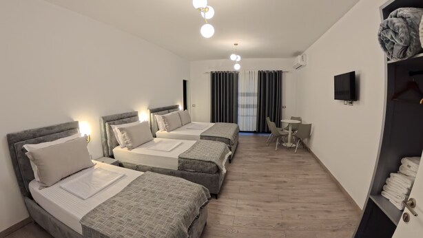 Ein Hotelzimmer mit drei Betten, einem kleinen Tisch, einem Fernseher und einem Kleiderschrank.