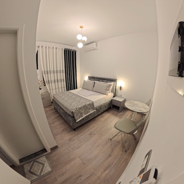 Un dormitorio moderno con cama, mesita de noche, silla y una pequeña mesa redonda.