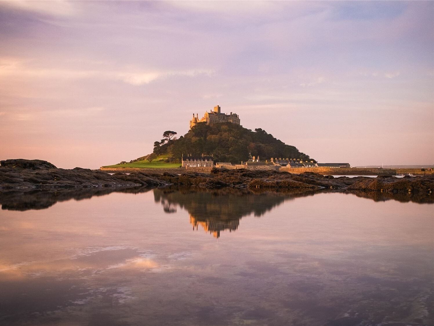 A castle on a rocky island with a calm lake in the foreground.