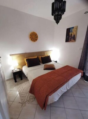 A bedroom with a bed, bedside tables, a wall clock, and a painting. - L'Oranger | Cosy air-conditioned apartment 3 min from the Souk, near Agadir beach (Agadir)