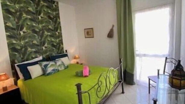 Een kamer met een bed, een tafel, een stoel, een lamp en een raam met gordijnen.