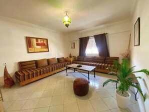 A living room with a sofa set, a coffee table, a potted plant, and a painting on the wall. - Charming Le Palmier apartment - Close to the beach, Souk El Had and the town center (Agadir)