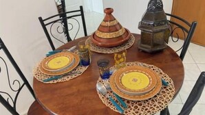 Een ronde houten tafel met vier stoelen, een Marokkaanse tajine, een lantaarn en decoratieve borden.