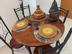 A round wooden table with four chairs, a Moroccan tagine, a lantern, and decorative plates. - Charming Le Palmier apartment - Close to the beach, Souk El Had and the town center (Agadir)