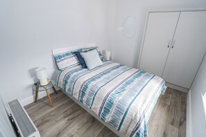 Ein Schlafzimmer mit Bett, Kleiderschrank, Nachttisch mit Lampe und Heizkörper.