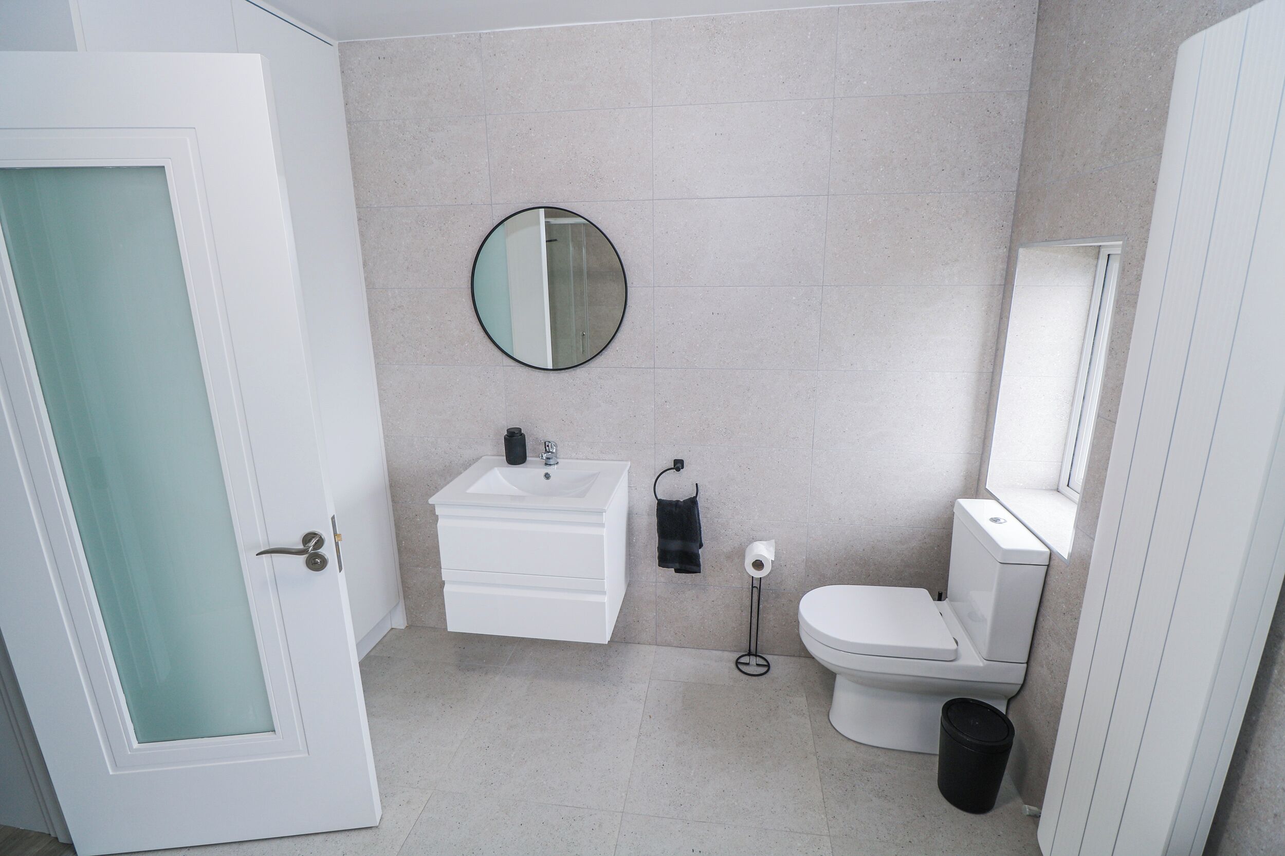Ein Badezimmer mit weißem Waschbecken, Spiegel, Toilette und Mülleimer.