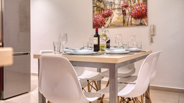 Un comedor con una mesa dispuesta para cuatro personas, un refrigerador y un cuadro en la pared.