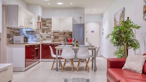 Una cocina moderna con armarios blancos, encimera roja y una zona de comedor con sillas blancas.
