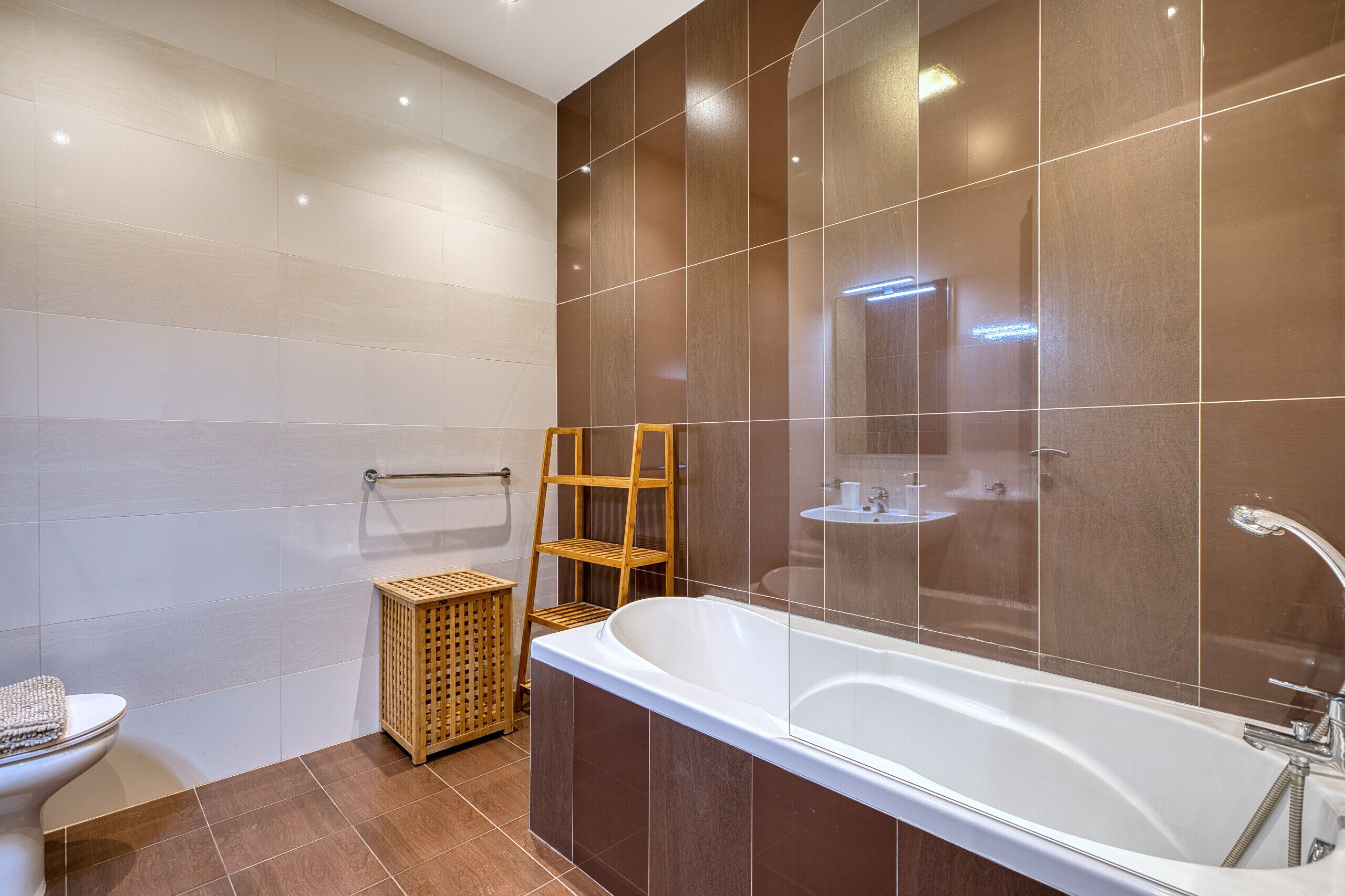 Een moderne badkamer met een bad, toilet, een houten plank en een rieten mand.