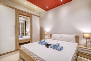 A hotel room with a bed, a wardrobe, a nightstand, and a lamp. - Modern 2 bedroom flat with yard in Sliema NBOR1-1 (Sliema)