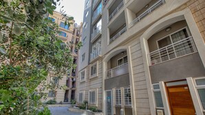 Un edificio residencial de varios pisos con balcones, entrada protegida por un portón y un pequeño jardín.