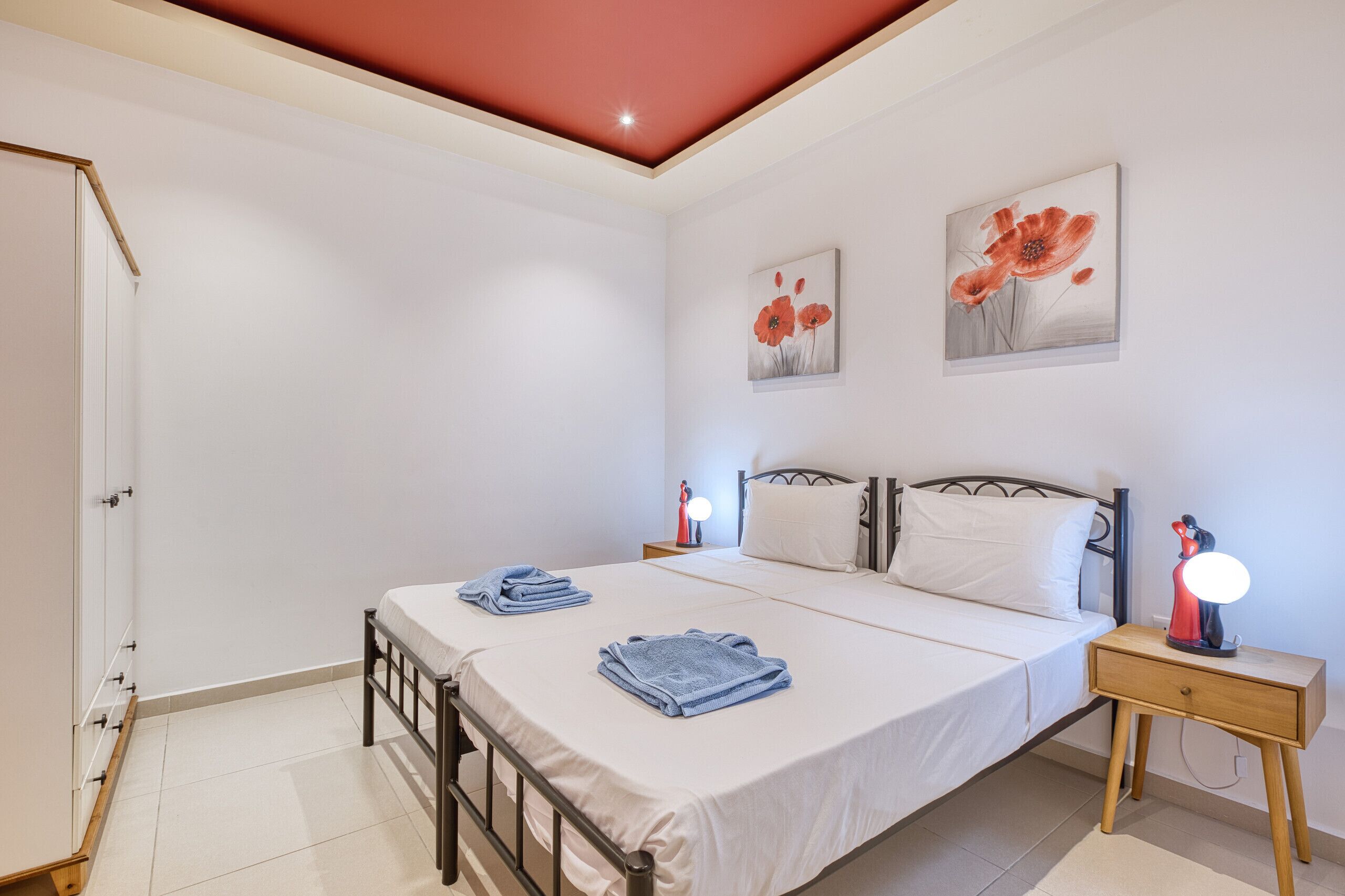 Une chambre à coucher comprenant un lit, deux tables de chevet, une commode, une porte et deux tableaux accrochés au mur.