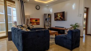 A living room with a sofa set, a coffee table, a bookshelf, a flat-screen TV, and a painting. - 3-bedroom seaview apartment in Mombasa, close to the beach, with AC (Mombasa)