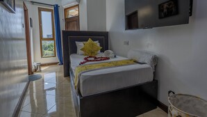 A hotel room with a bed, a TV mounted on the wall, and a window with curtains. - 3-bedroom seaview apartment in Mombasa, close to the beach, with AC (Mombasa)