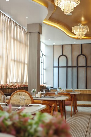 Ein Restaurantinneres mit runden Tischen, Stühlen und einem großen Fenster mit Vorhängen.