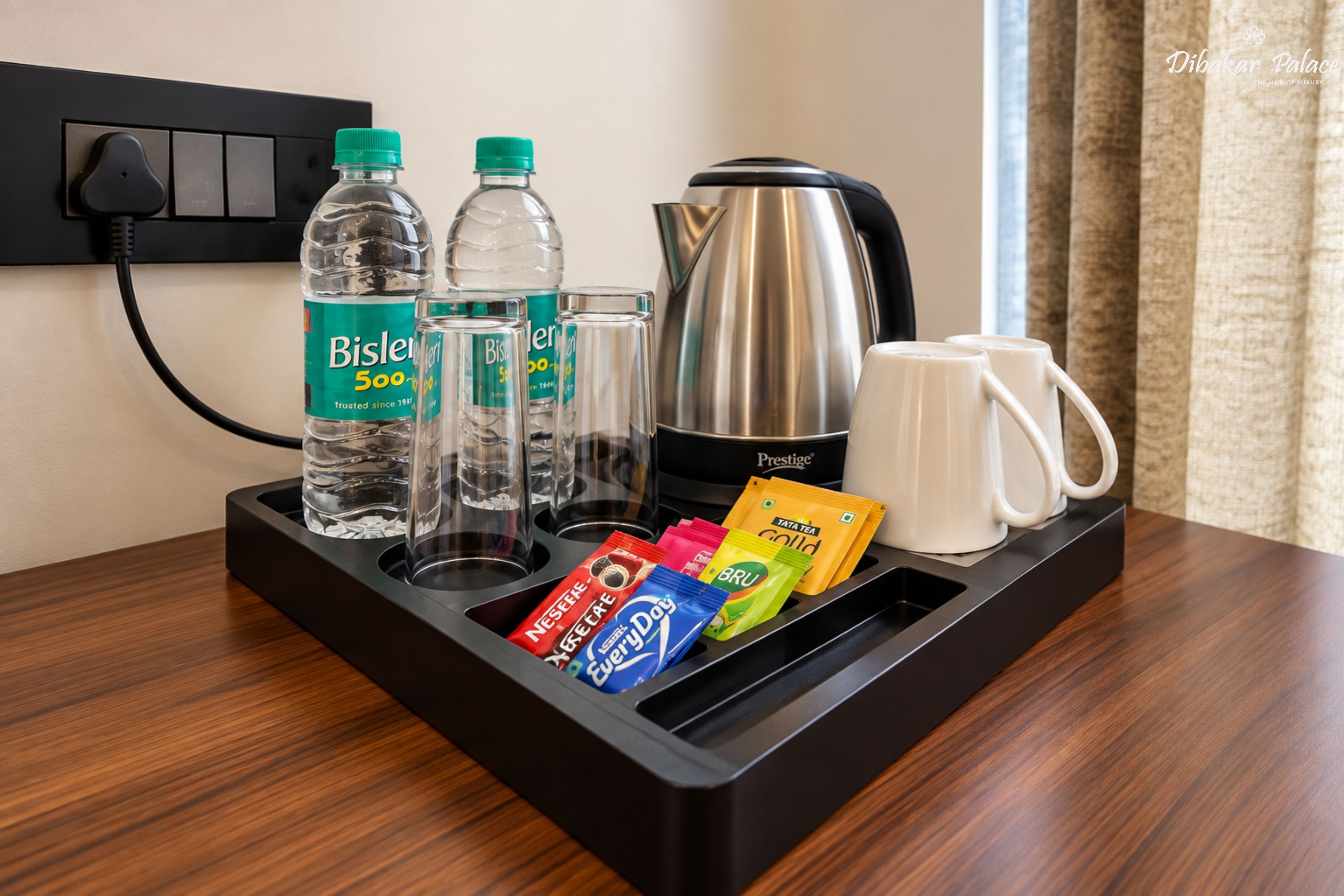 A hotel minibar with Bisleri water bottles, glasses, a Prestige coffee maker, and tea packets.