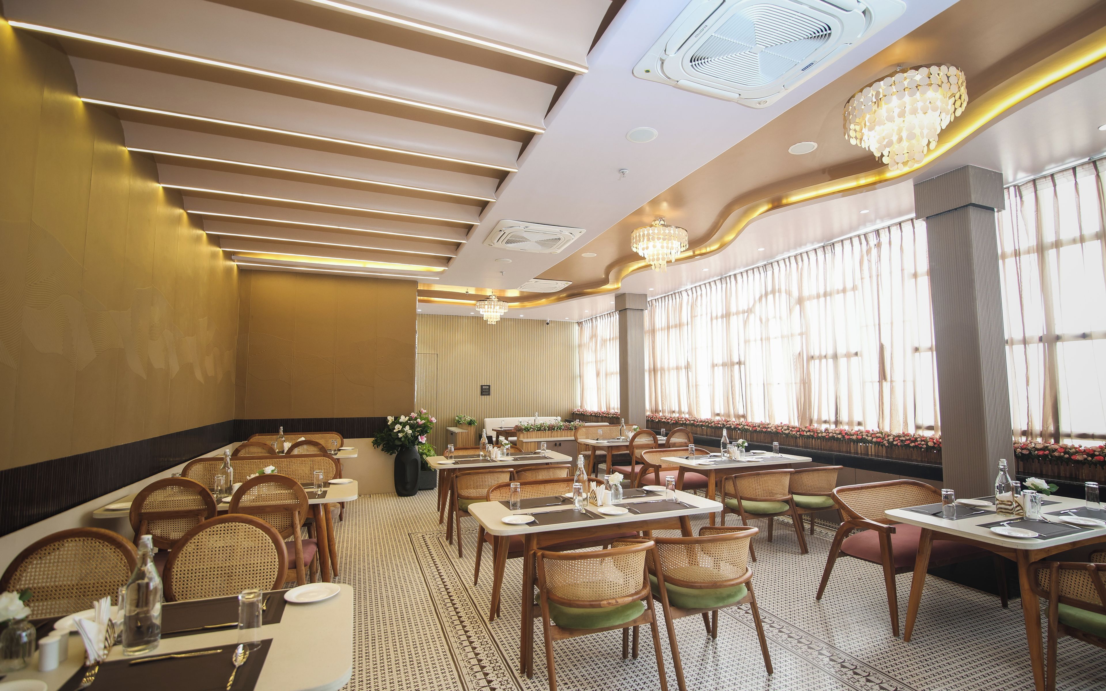 Restaurante com várias mesas e cadeiras, ventiladores de teto e grandes janelas com cortinas.