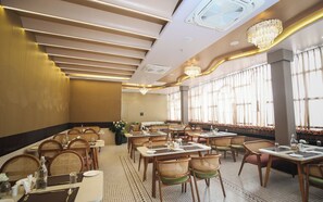 A restaurant with multiple tables and chairs, ceiling fans, and large windows with curtains. - Dibakar Palace (Tezpur)