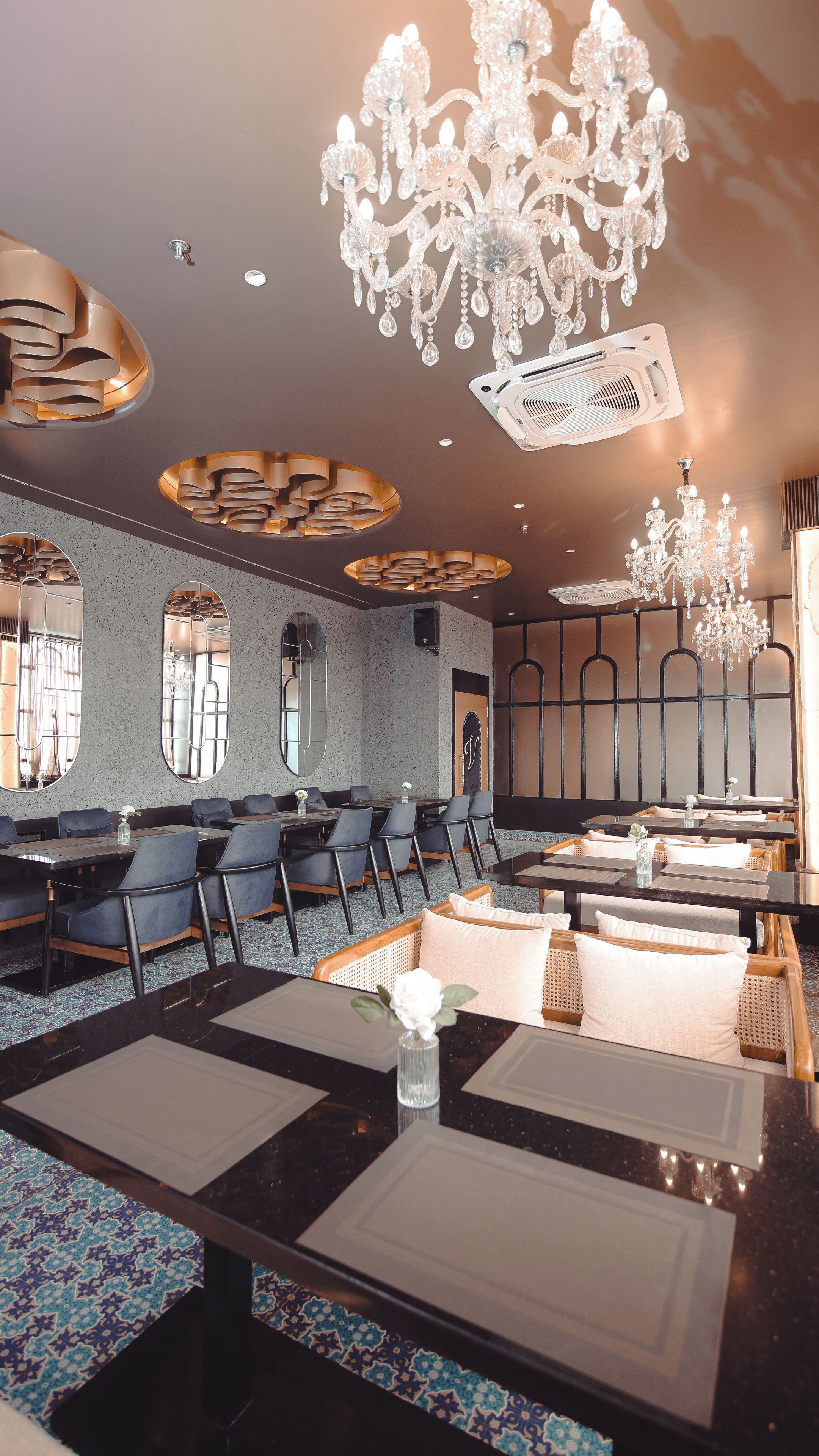 A hotel dining area with multiple tables, chairs, and a chandelier.